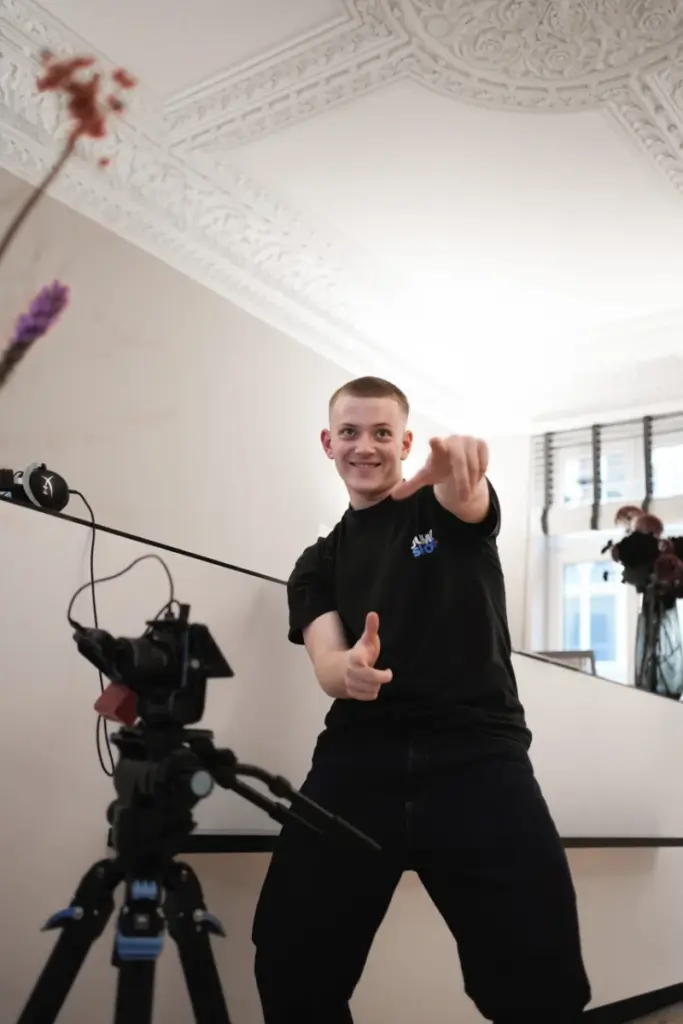 Lächelnder Mann gestikuliert vor eleganter Kulisse. Kamerastativ im Vordergrund, ideal für Social Media Agentur Fotoshootings.