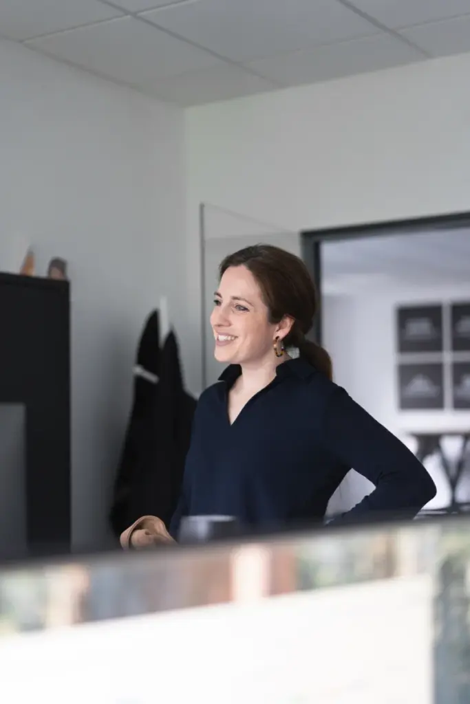 Brahnhaarige Frau lächelt bei der Arbeit an einer Theke in einer hellen Agentur in Paderborn.